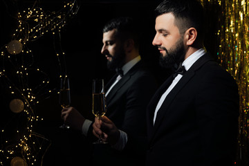 Successful handsome man in classic suit holds a glass of champagne. Bearded man in classic suit having luxury style. Merry Christmas and a happy new year 2020. Reflected in the mirror