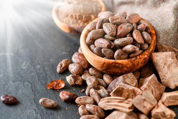 Cocoa raw beans in bowl and dark chocolate on black stone table.