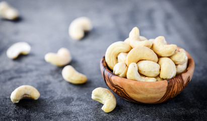 Cashew nuts in wooden bowl on dark stone table.