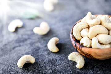 Cashew nuts in wooden bowl on dark stone table.