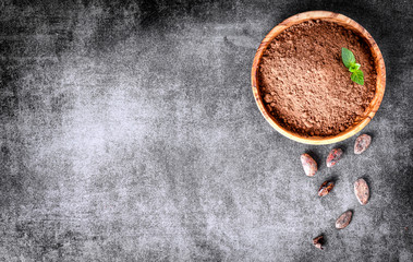 Cocoa beans and chocolate cacao powder with mint on top view. Copy space for text, dark stone table.