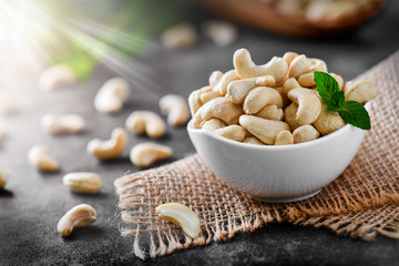 Cashew nuts in porcelain bowl on dark black table with mint leaf on top. Raw cashews side view.