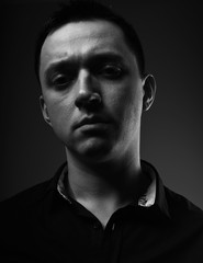 Sexy young man looking serious in black shirt on grey studio dark shadow background. Closeup portrait. Art.