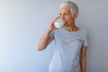 Senior Woman Holding Glass Of Milk At Home. Middle age woman drinking a glass of fresh milk with a happy face standing and smiling with a confident smile showing teeth