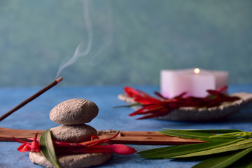 Relaxation and spa concept. Water style background, stacked stones in equilibrium, incense and lit candle, leaves and petals in stone bowl. Blue, green, red and stone gray colors. Natural light.
