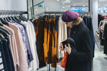 Beautiful French woman wearing purple beret hat looking at the orange leather purse in fashionable clothing store - Powered by Adobe