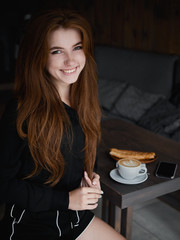 Cute redhead woman woman with adorable smile sitting in cozy city cafe enjoying free time coffee break with cappuccino and dessert dressed black blouse and shorts