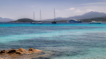 Fototapeta premium Sardinia, Italy, holidays. Sea with crystal clear azure water, yachts and ships in the sea, mountains in the background.