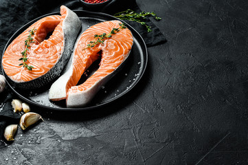 Raw salmon steak on a plate with spices. Atlantic fish. Black background. Top view. Space for text