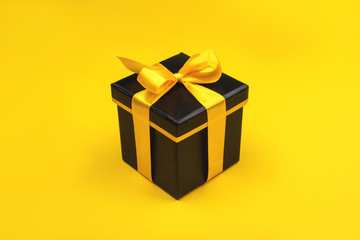 One black gift box on yellow background. Holiday concept.