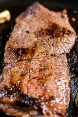 Strip loin steak in a frying pan. Grilled meat. Black background. Top view