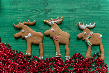 Festive, decorated gingerbread raindeer cookies on green wooden background. Christmas decorated, greeting cards concept with red pearls and space for text