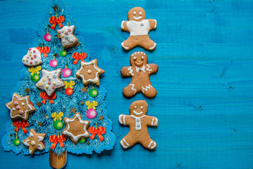 Christmas homemade gingerbread man cookies, on blue wooden background with decorated blue Christmas tree. Greeting card concept