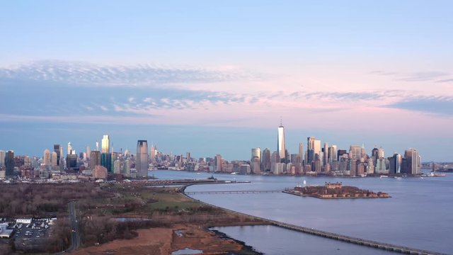 Aerial footage of New York City and Jersey City skylines together with Ellis Island, as viewed from above Liberty State Park, in New Jersey, at dusk, with slow forward camera movement.