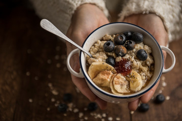 Woman hands offering a vegan brunch, porridge with oat flakes, banana, blueberries, chia, cinnamon, maple syrup and strawberry jam. Horizontal. Top view. Copyspace