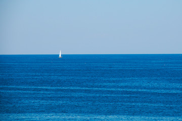 White sailboat on blue ocean horizon with blue sky
