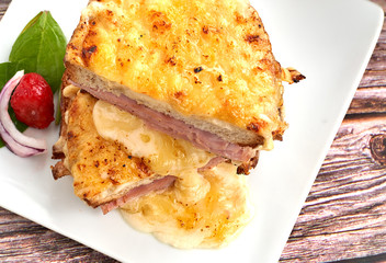 Sandwich with Parmesan and Gruyere cheese, ham, béchamel sauce and artisan bread accompanied by a salad on a wooden background.  The Croque Monsieur.