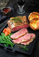 Traditional Commonwealth Sunday roast with sliced cold cuts roast beef with vegetable and Yorkshire pudding as closeup on a modern design cast iron tray