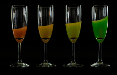 4 glasses with coloured liquid on black background