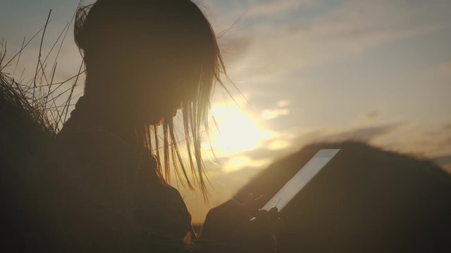 Girl farmer uses tablet in the field next to haystack at sunset. Smart farming, using modern technologies in agriculture.
