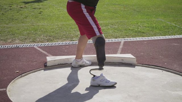 A young athlete on the prosthesis pushes the core in the stadium. A disabled person is preparing for the competition. The core thrower with an amputated leg.