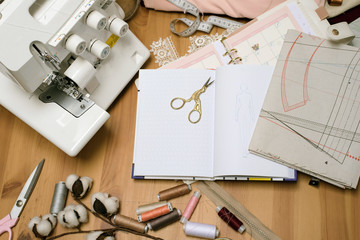 Wooden table of seamstress with scattered scissors, an overlock, a sewing machine, drawings,...