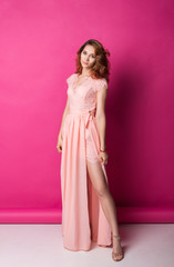 Slim pretty redhead woman in pink dress over studio background