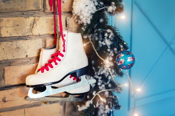 Pair of white vintage leather skates with red laces hanging on old rustic brick wall with garland lights on christmas tree decoration. Cozy scenic christmas card interior winter holidays background