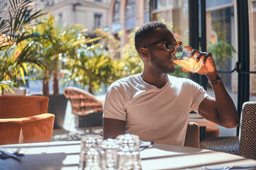 American student is drinking fruit juice at cafe on hot sunny day.