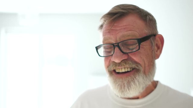 Portrait of an elderly happy pensioner with glasses with a gray beard and a white T-shirt. Happy retirement