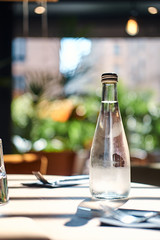 On a sunny day at small restaurant cold bottle of mineral water is standing on the table.