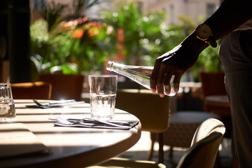 Man with watch on his wrist is pouring fresh water to the glass.