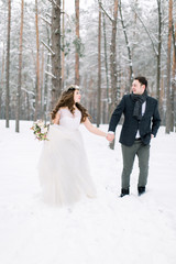 Fototapeta na wymiar Winter wedding in a snowy forest, lovely couple holding hands, looking each other, walking outdoors in winter forest
