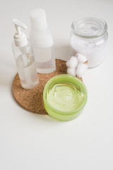 Home skin care, micellar water, creams and a candle with a cotton flower on the bedside table. White body and skin care cosmetics in a white modern bathroom on a shelf, copy the space