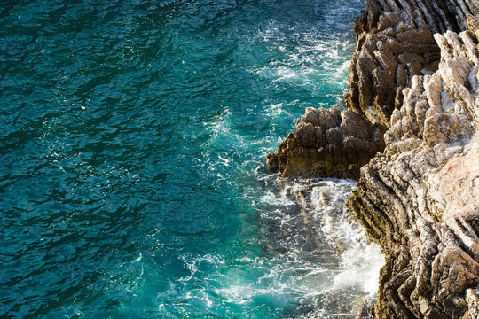 Waves crashing on rocky cliff with white spray and foam on deep blue sea water.