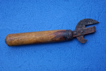 old rusty can opener with a brown wooden handle lies on a blue table