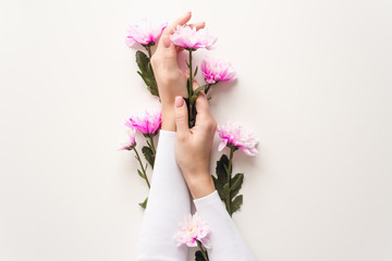 Hands of a girl with a nude manicure in flowers on a white background with pink chrysanthemums. The concept of caring for the skin of hands. Natural cosmetics from flower extract, beauty and fashion