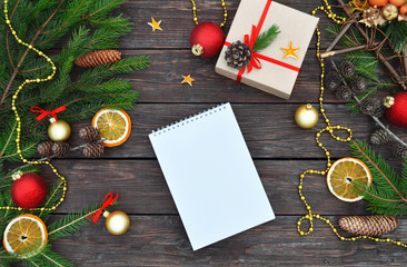 Christmas or New Year composition with notepad, festive decorations, gift box, fir branches and cones on a vintage wooden background with copy space. Top view.