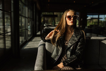 beautiful girl model in a restaurant in a beautiful loft interior. on the eyes of sunglasses, dressed in a leather black jacket, casual clothes. warm photography, sunlight
