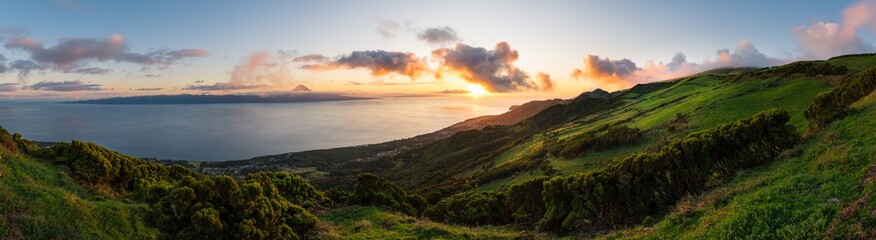 Panoramic view of an Azores sunset across the hilly S&atilde;o Jorge countryside with Pico Island across the sea in the background with the summit of Mount Pico visible on the horizon within dramatic clouds.