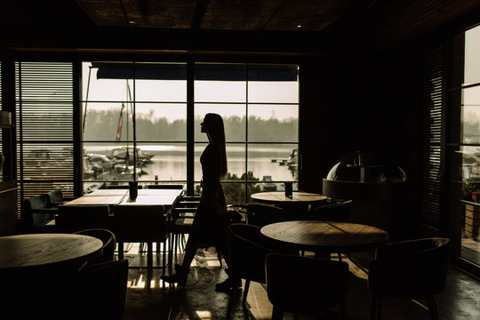 Silhouette Of A Young Stylish Girl In Sunglasses Walking Along A Panoramic Window. On the background of the yacht. Business woman