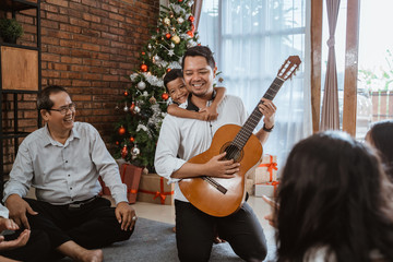 family and friend singing a song together. father playing guitar during christmas