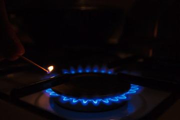 Gas burner on white modern kitchen stove. Kitchen gas cooker with burning fire propane gas. A man lighting the gas-stove with a match.