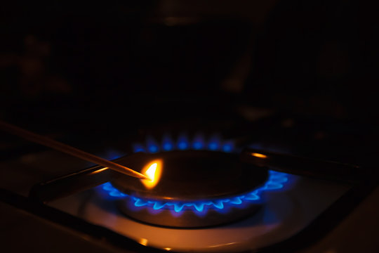 Gas Burner On White Modern Kitchen Stove. Kitchen Gas Cooker With Burning Fire Propane Gas. A Man Lighting The Gas-stove With A Match.