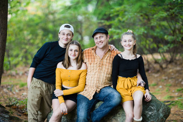 Fototapeta premium White Caucasian family father and teenager son and daughter sitting on the rock at fall forest