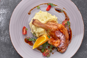 Cooked duck leg in sauce, with mashed potatoes, on a dark background