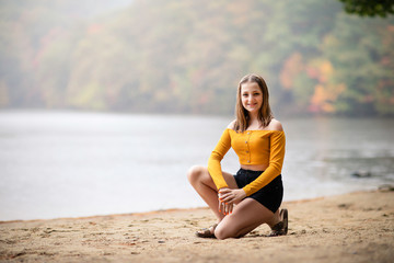 Fototapeta na wymiar Beautiful teenager girl sitting on the beach front of the lake. Fall season. Family photography