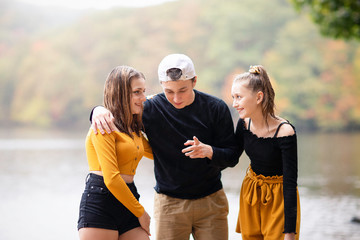 Three teenagers friends, sisters and brother sitting on front of the lake. Fall season. Family photography
