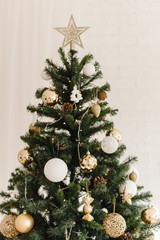 The top of a Christmas artificial tree standing at home. Beige golden shiny star at the top of the tree. Decorating a Christmas tree with beige, gold and white Christmas balls and decorations