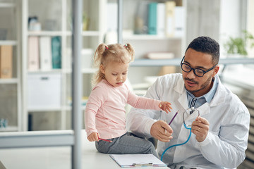 Obraz premium Portrait of African-American doctor examining cute little girl in modern clinic, copy space
